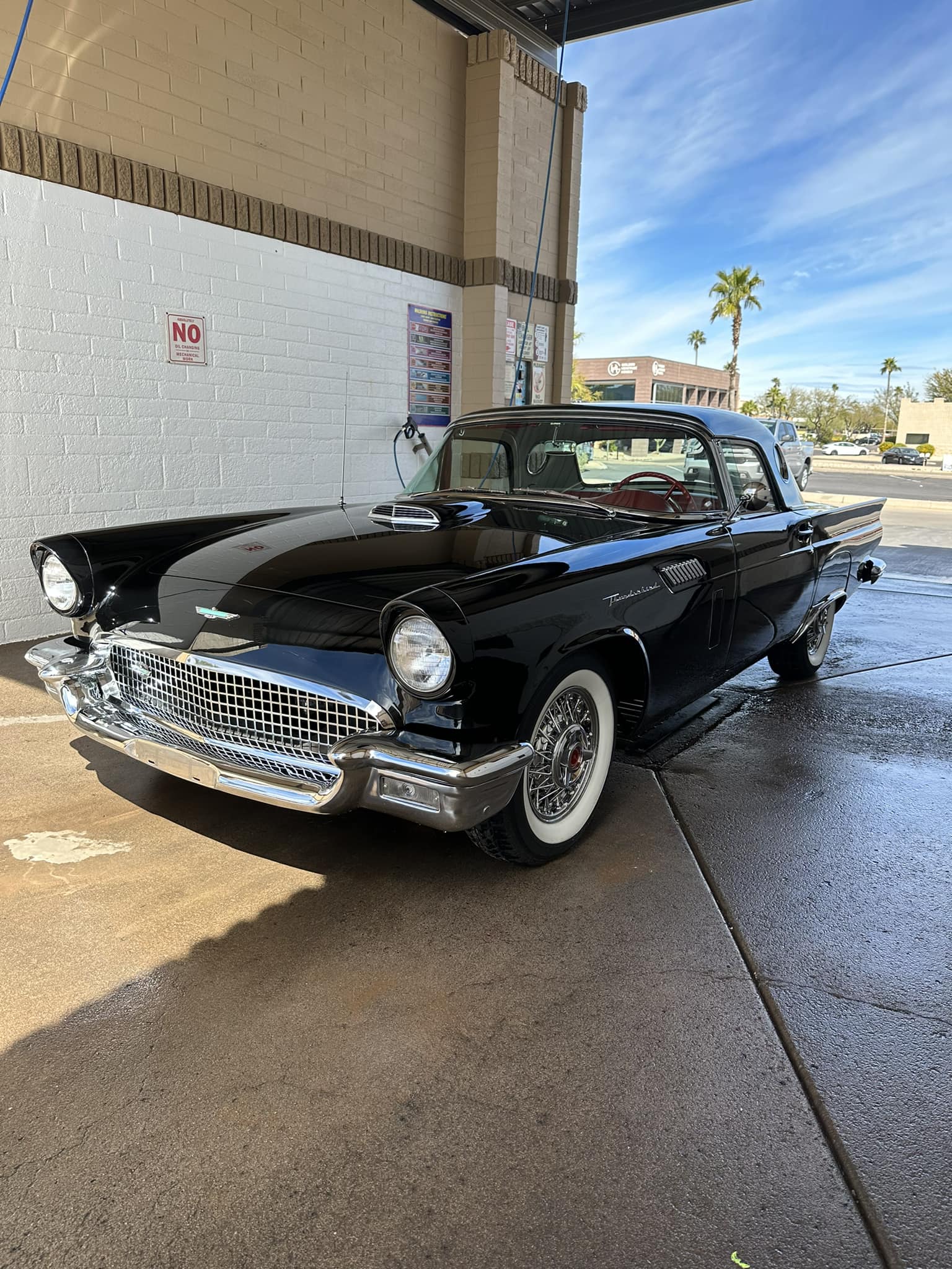 Shiny black vintage Ford Thunderbird with whitewall tires parked in a car wash bay.