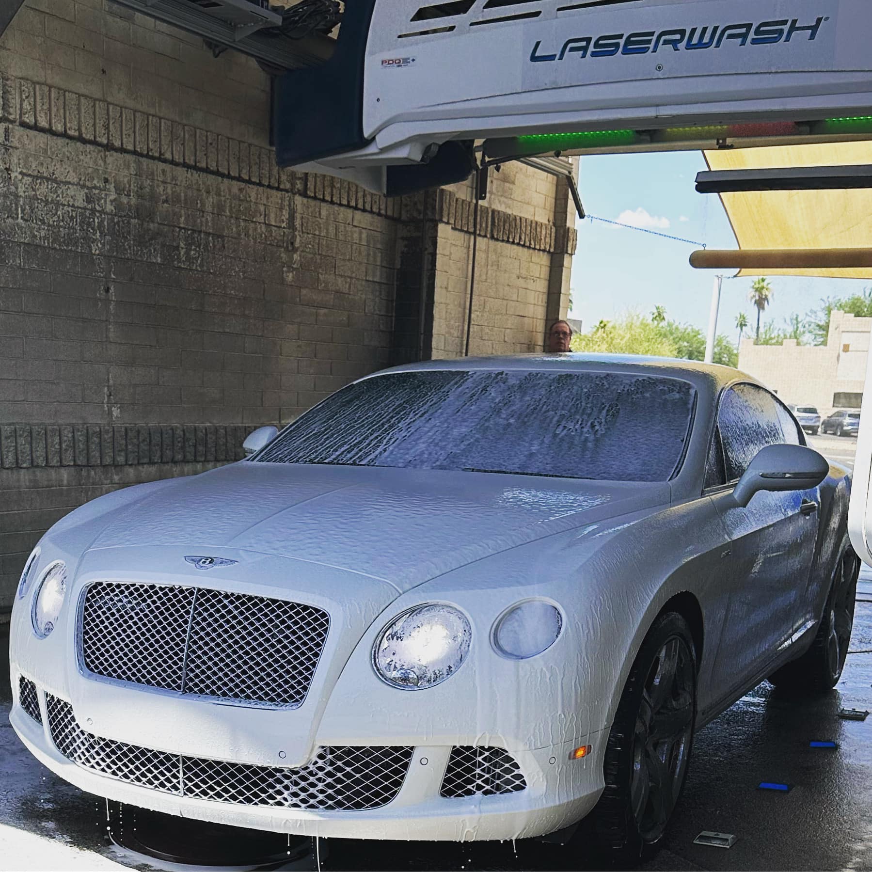 White Bentley luxury car covered in soap foam inside an automatic LaserWash car wash.
