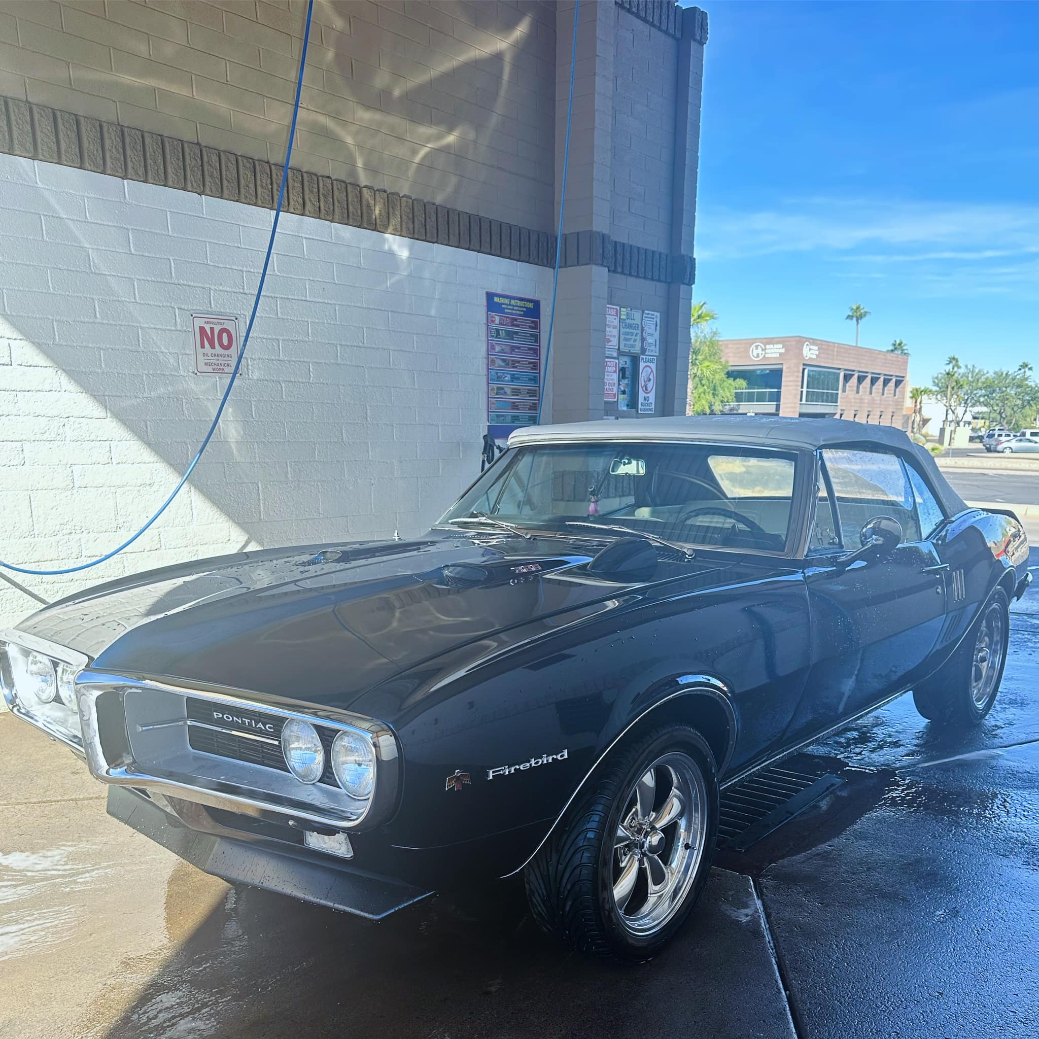 Shiny black classic Pontiac Firebird convertible with a white top at a car wash.