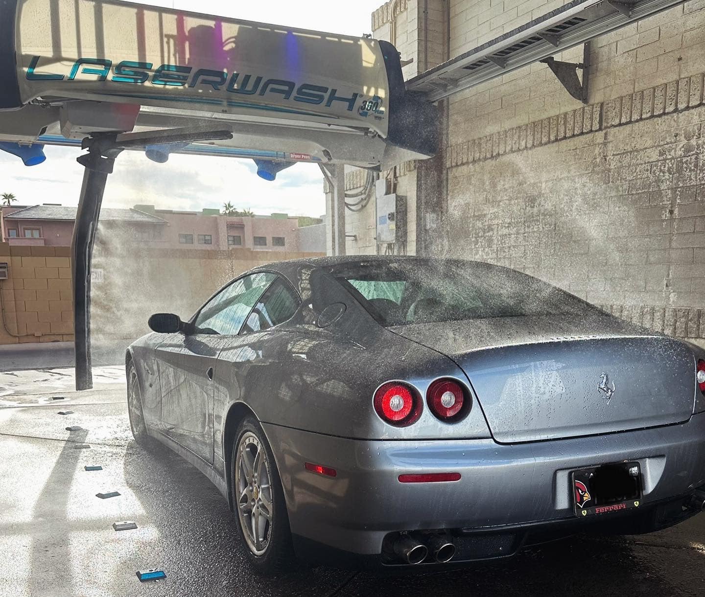 Silver Ferrari sports car being sprayed with water in an automated touchless car wash.