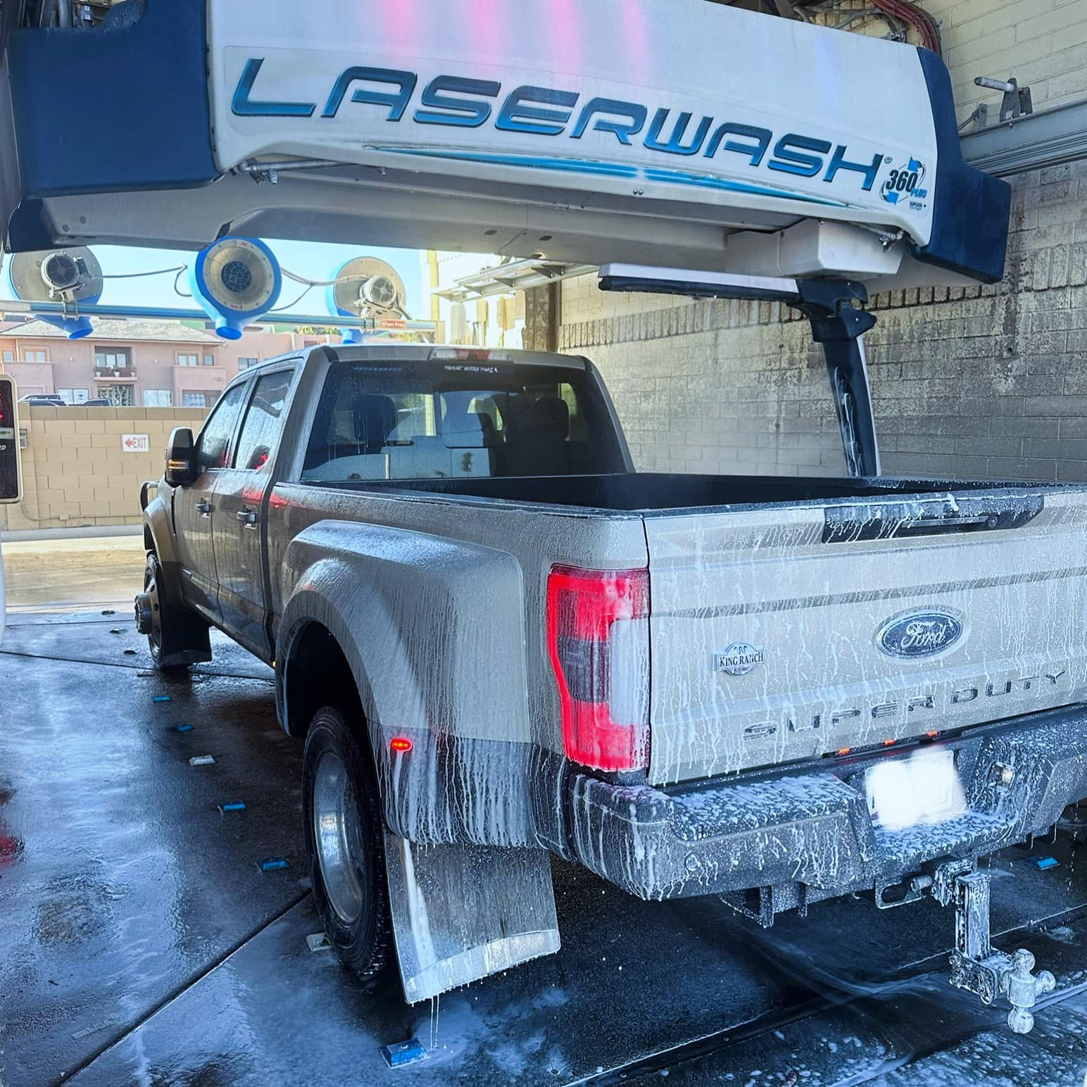 Silver Ford Super Duty dually truck covered in soap suds inside an automated LaserWash bay.