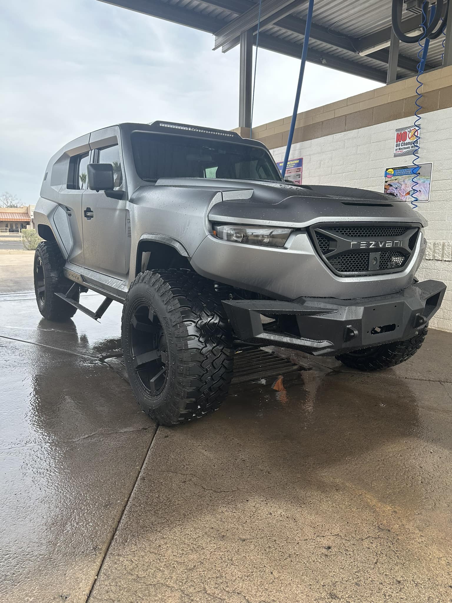 Silver Rezvani Tank SUV with large off-road tires parked in a wet car wash bay.
