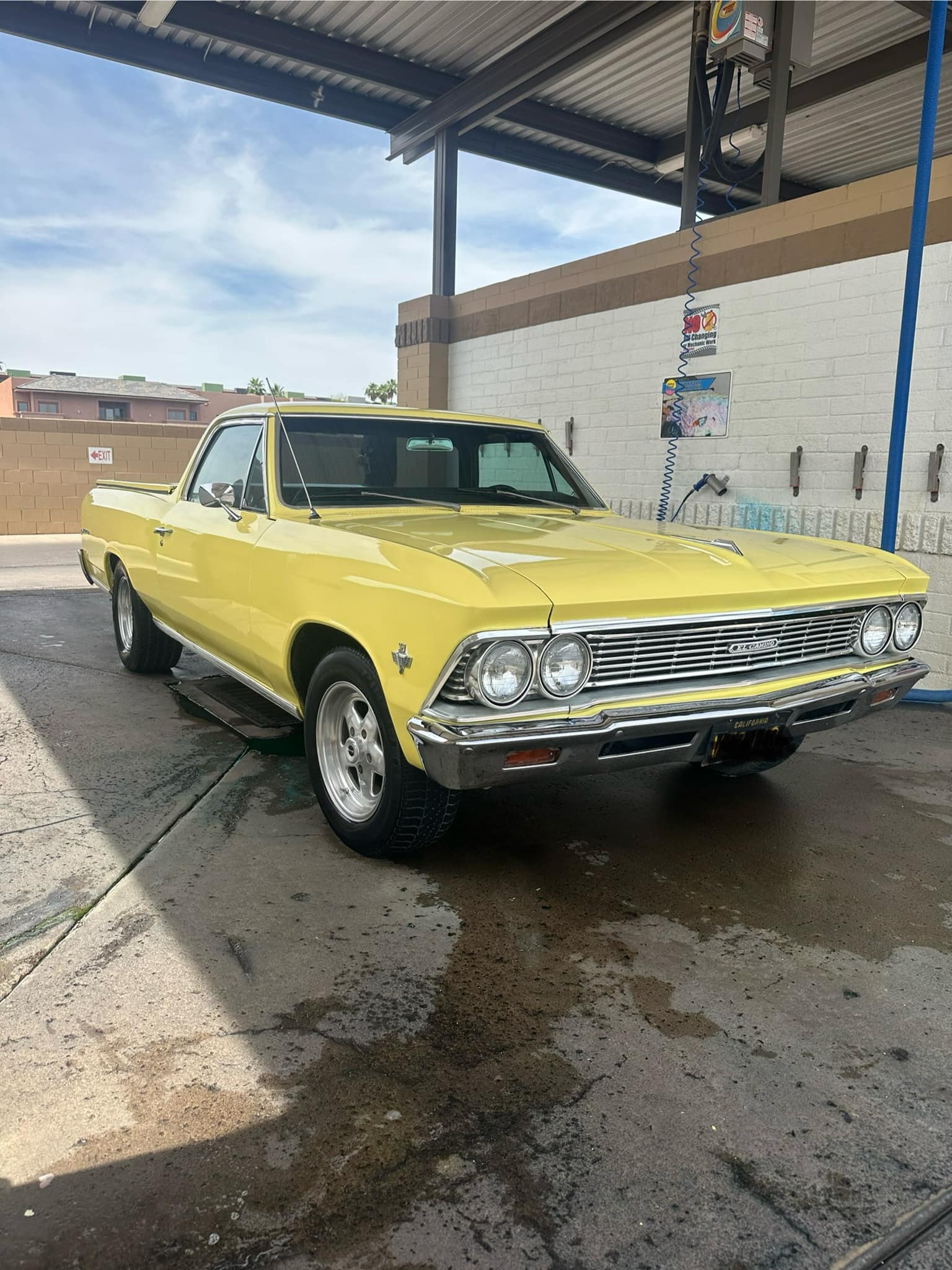 Bright yellow classic Chevrolet El Camino parked in a self-service car wash bay.