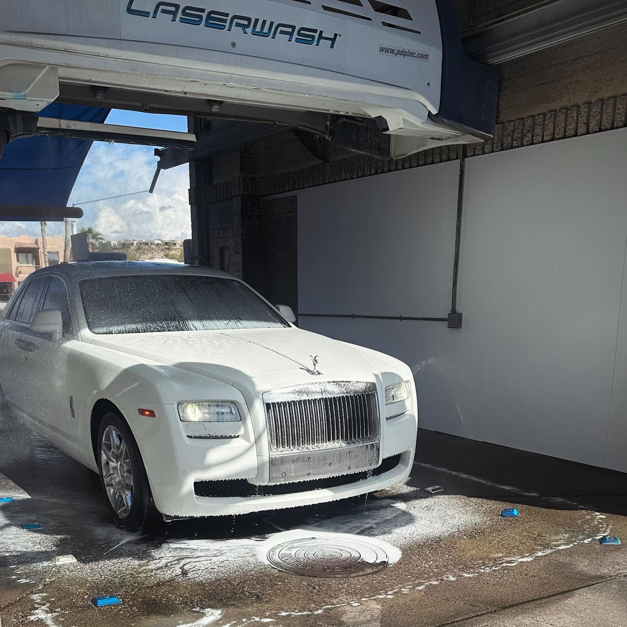 White Rolls-Royce Ghost luxury car covered in soap suds inside an automatic car wash.