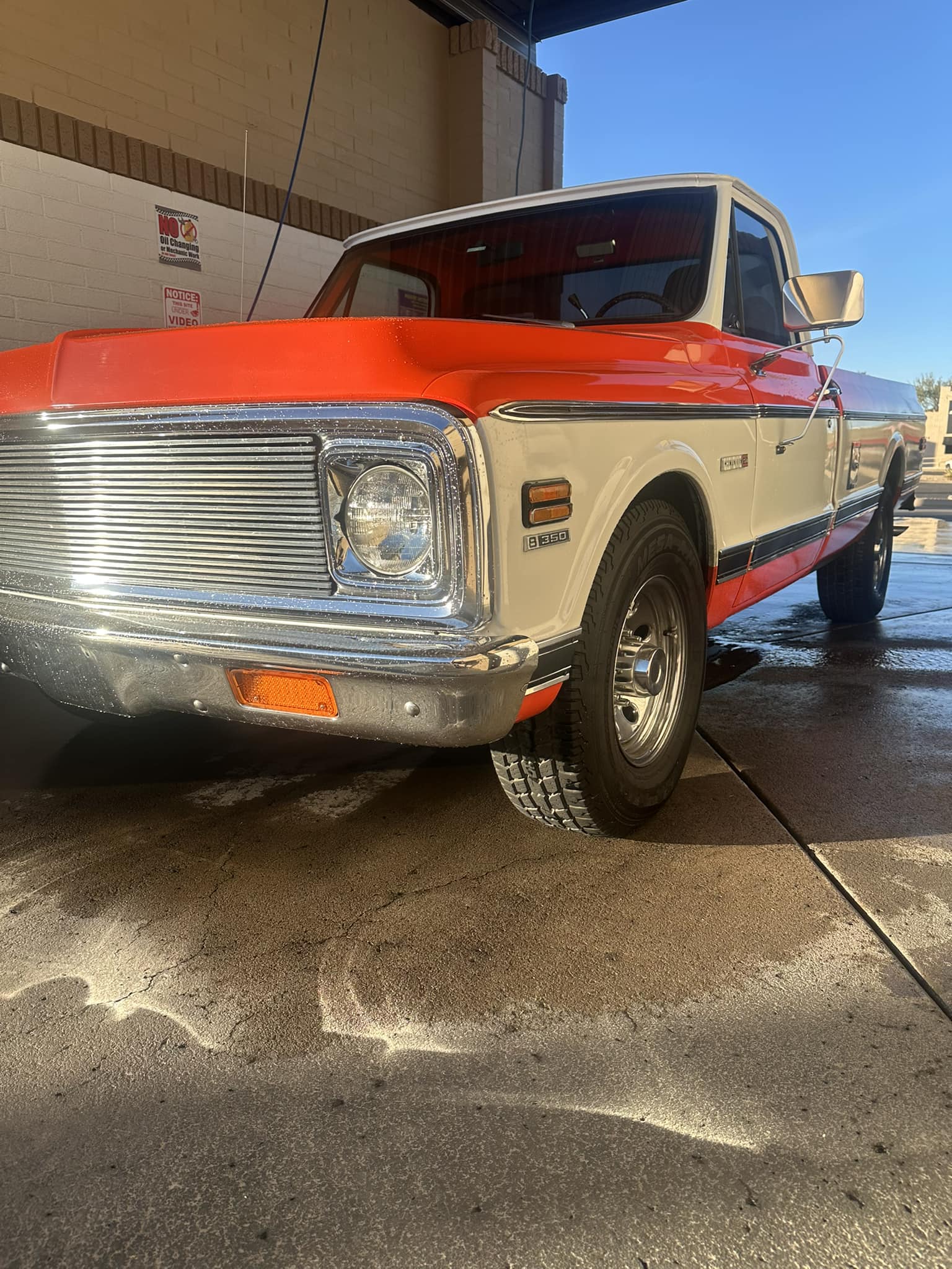 Vintage orange and white pickup truck with chrome grille parked in a wet car wash.