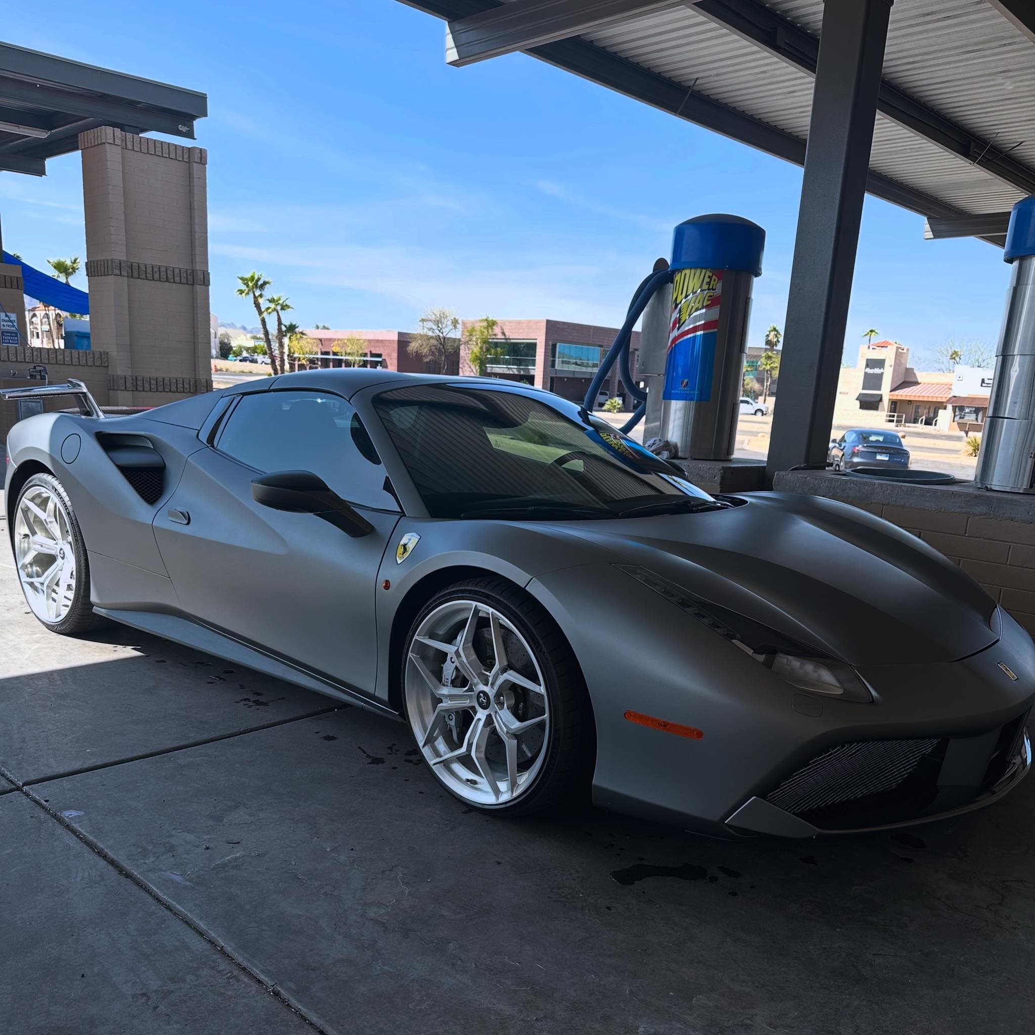 Matte grey Ferrari with silver multi-spoke wheels parked at a car wash vacuum station.