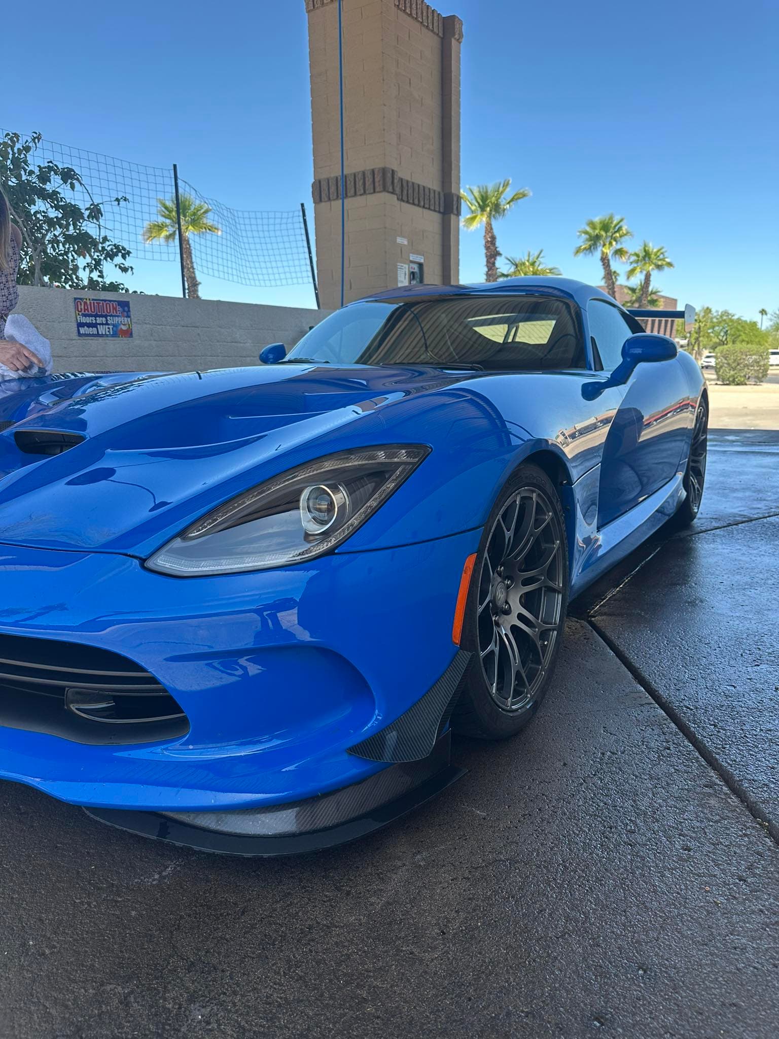 Bright blue Dodge Viper sports car with carbon fiber accents parked on wet pavement.
