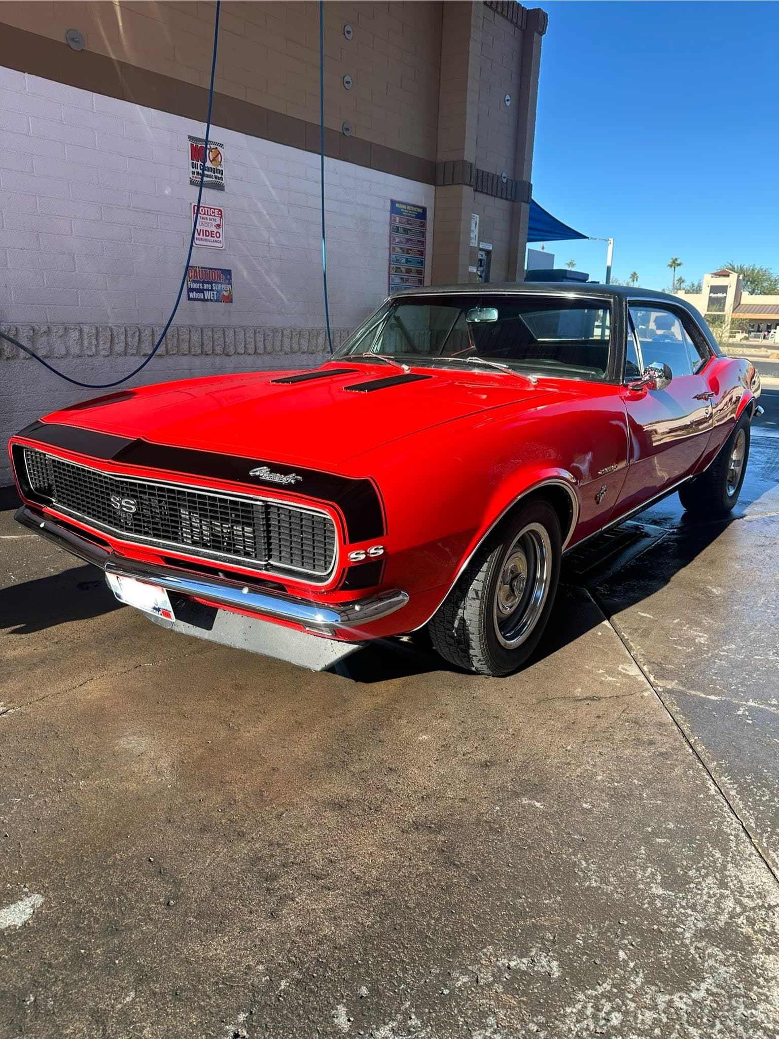 Vintage red Chevrolet Camaro SS with black stripes and chrome bumpers at a car wash.