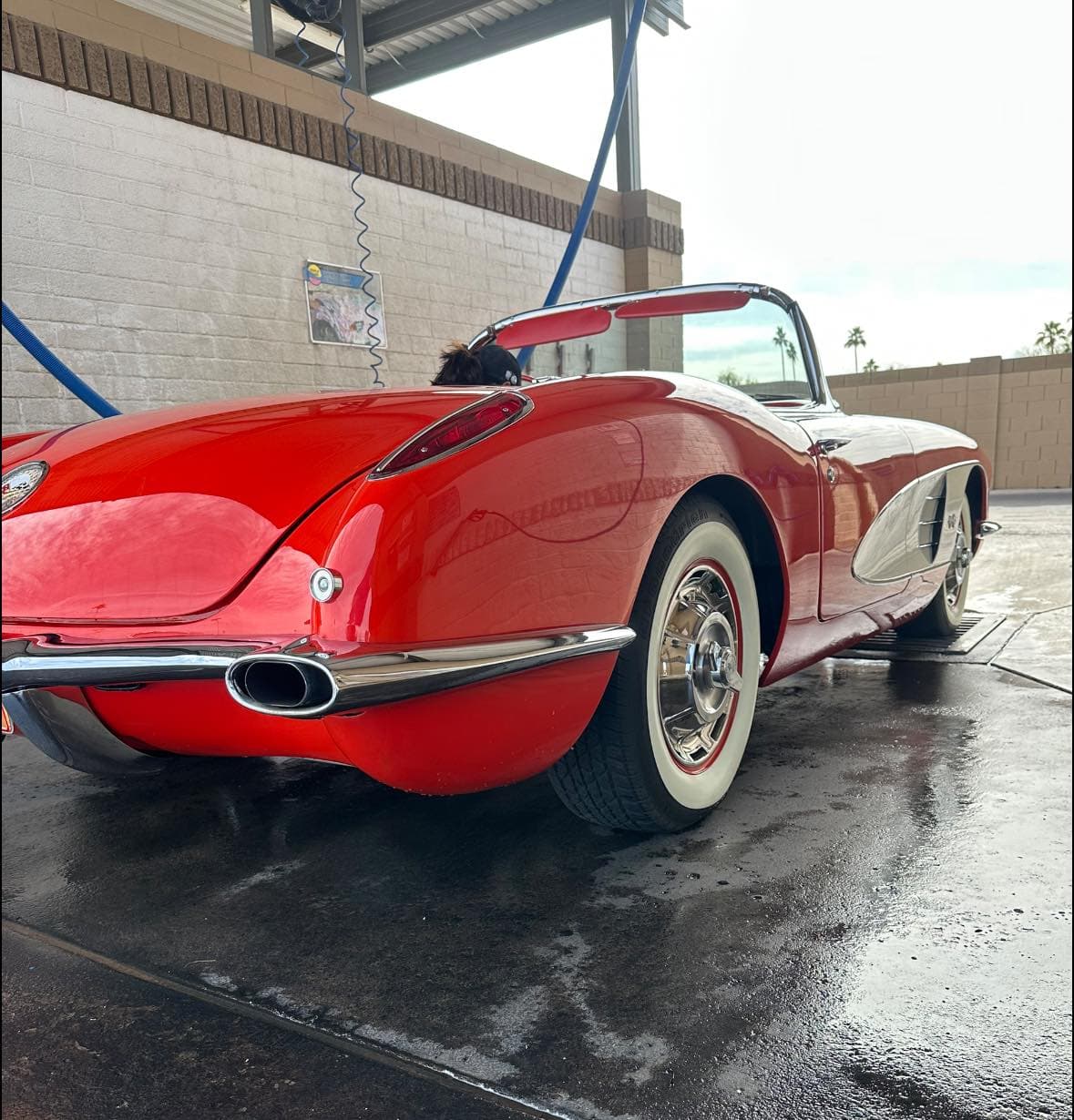 Classic red Corvette convertible with white-wall tires parked in a wet car wash bay.