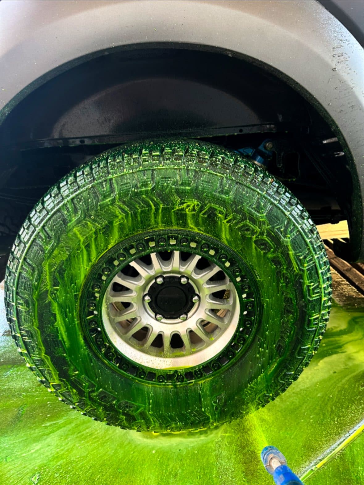 Neon green cleaning foam dripping down a rugged off-road truck tire during a wash.